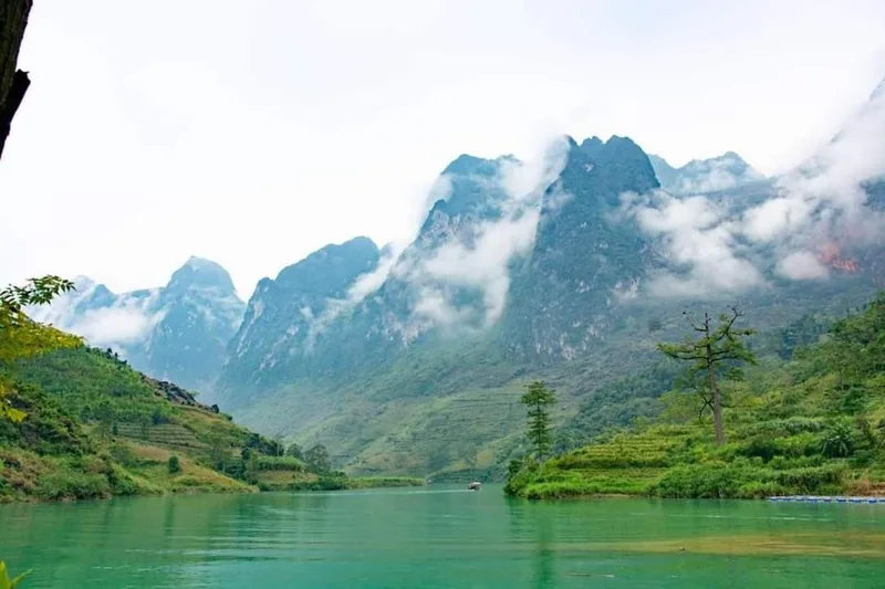 Mist wraps jagged limestone peaks above a turquoise river in Ha Giang province.