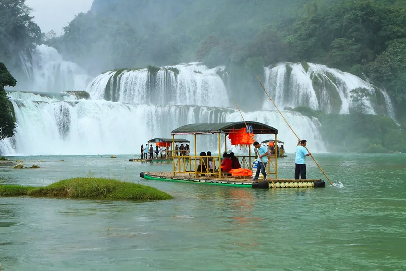 Bamboo rafts carry tourists across turquoise water before the wide cascades of Ban Gioc Waterfall.