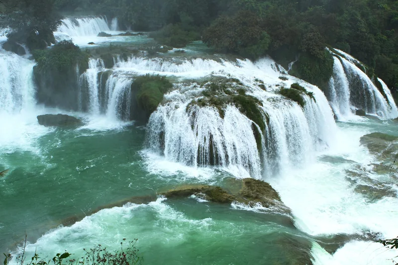 Tiered limestone terraces at Ban Gioc Waterfall in Cao Bang cascade into a turquoise river.