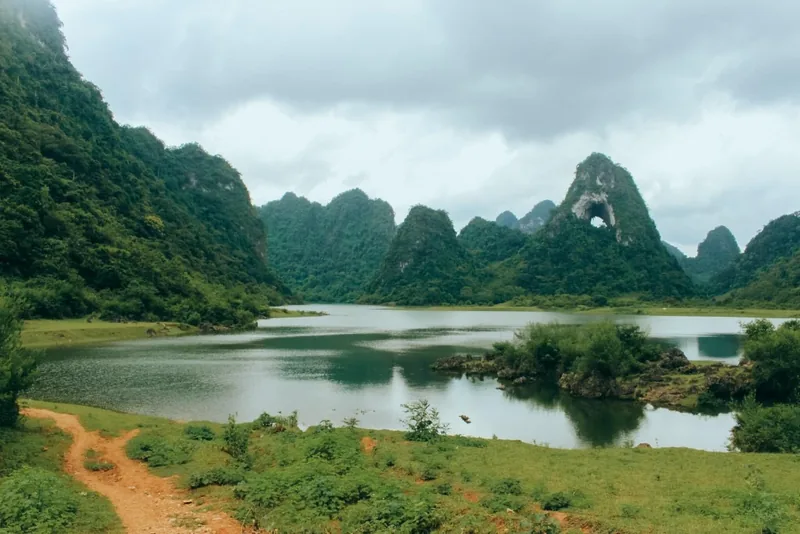 A calm lake reflects karst peaks, including one with a natural hole, near Cao Bang.