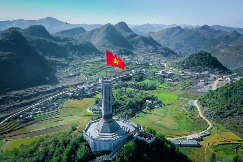 Aerial view of the Lung Cu Flag Tower flying a large Vietnamese flag amid the karst mountains of Ha Giang.