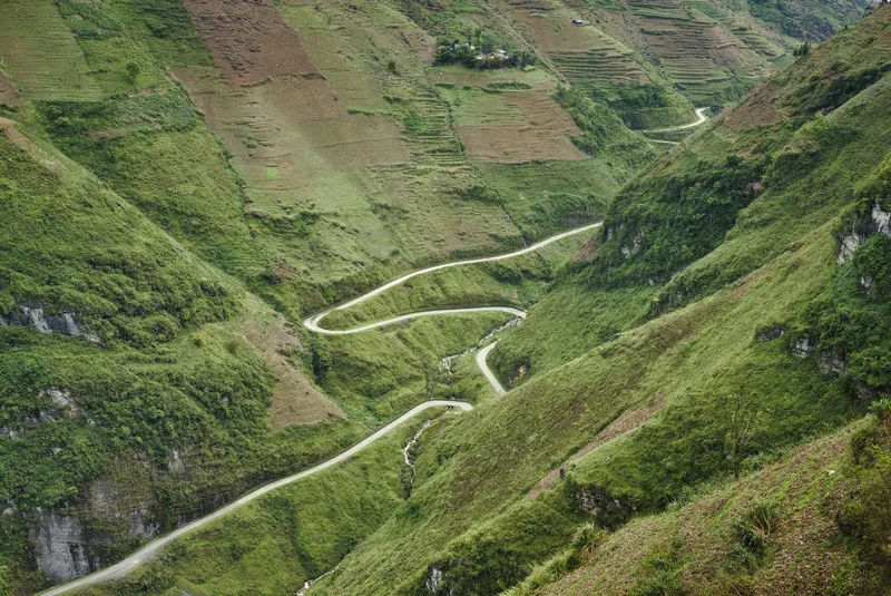 A winding mountain road snakes through the steep green valley of Ma Pi Leng Pass in Ha Giang.