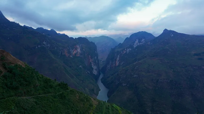 A river winds through the steep limestone walls of Tu San Canyon in Ha Giang under a dusky sky.