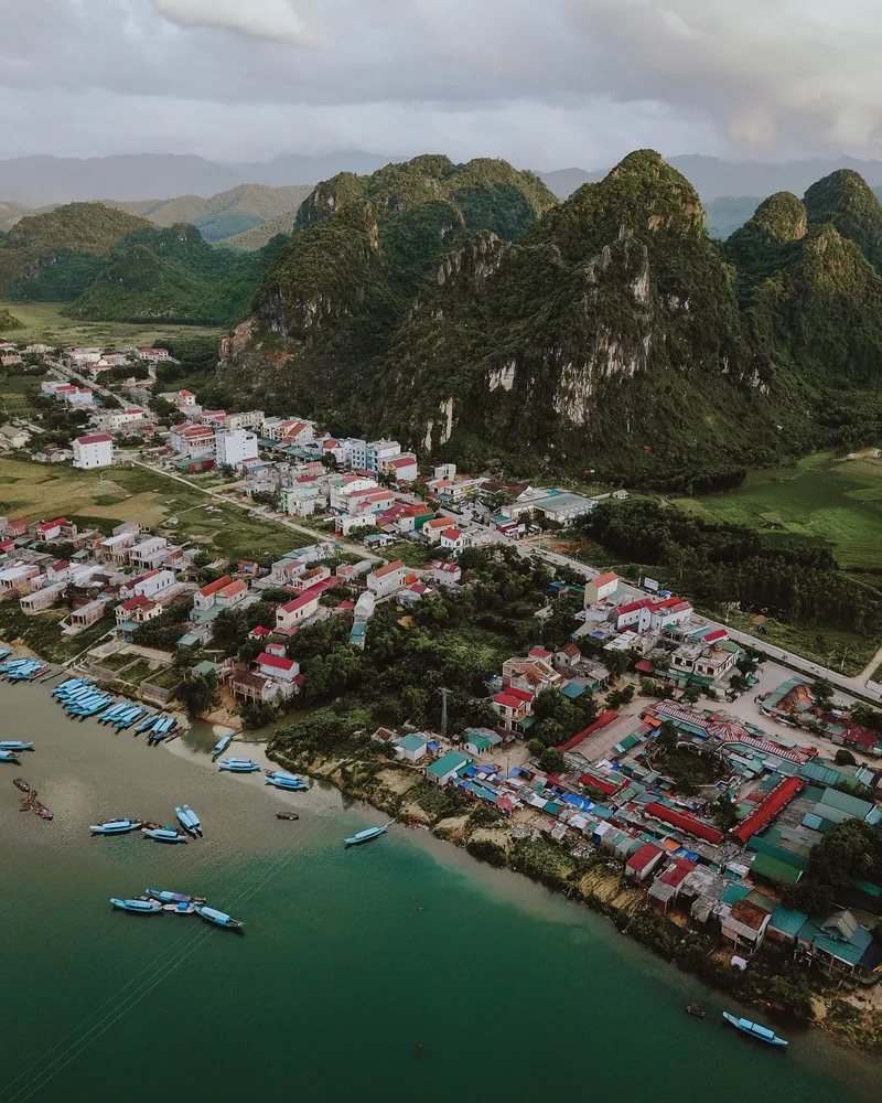 Aerial view of Phong Nha village nestled between limestone karst mountains and a green river with fishing boats.